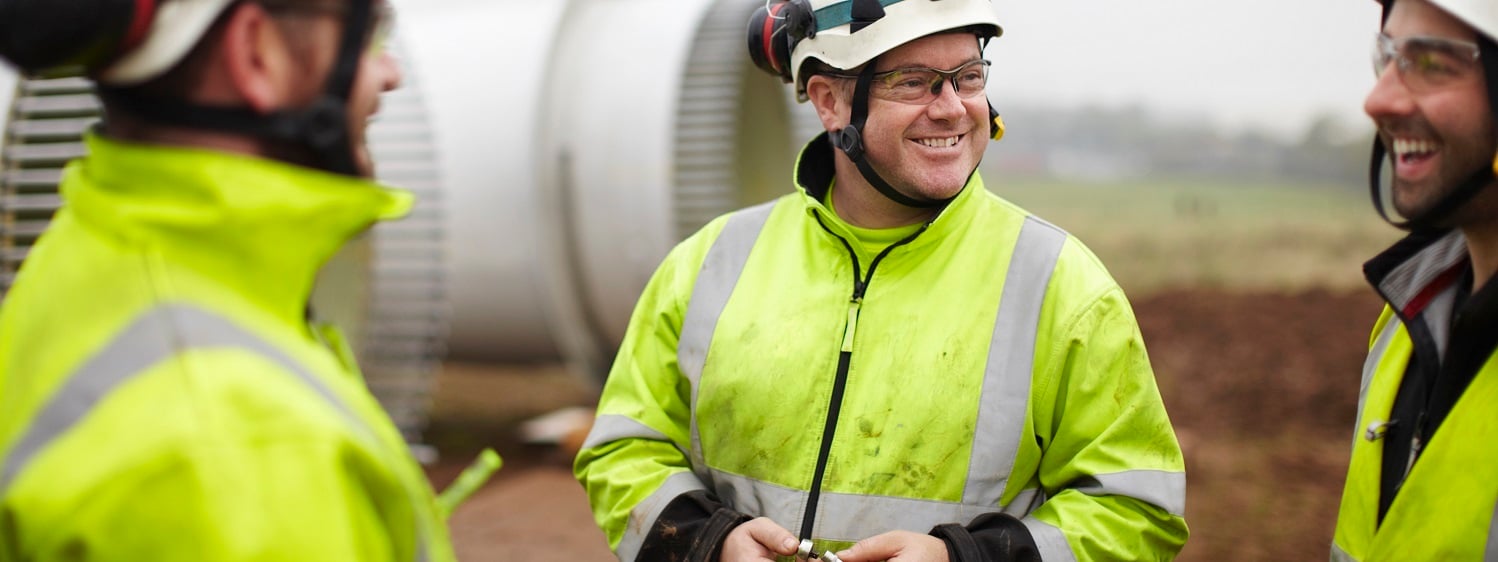 Three men in neon jackets talking at a wind farm