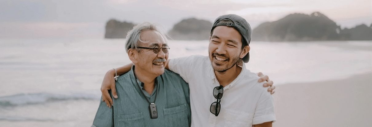 Son walking with senior father at the beach smiling.