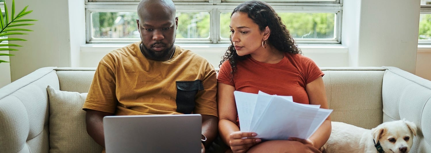 Man en vrouw zitten op de bank en kijken naar een laptop met hun hond.