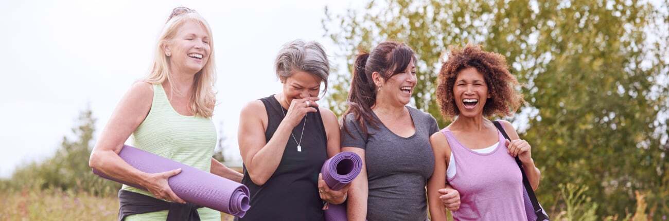 Group of midlife women outdoors with yoga mats, supporting each other during menopause