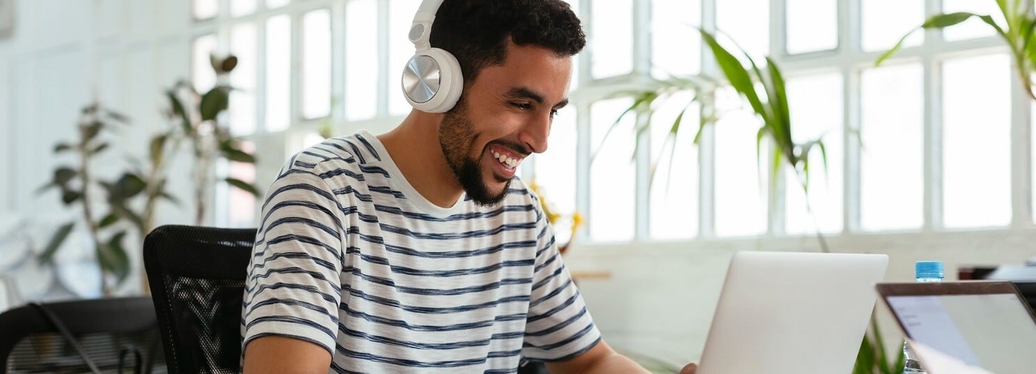 Homme-assis-au-bureau-avec-ordinateur-portable-et-écouteurs