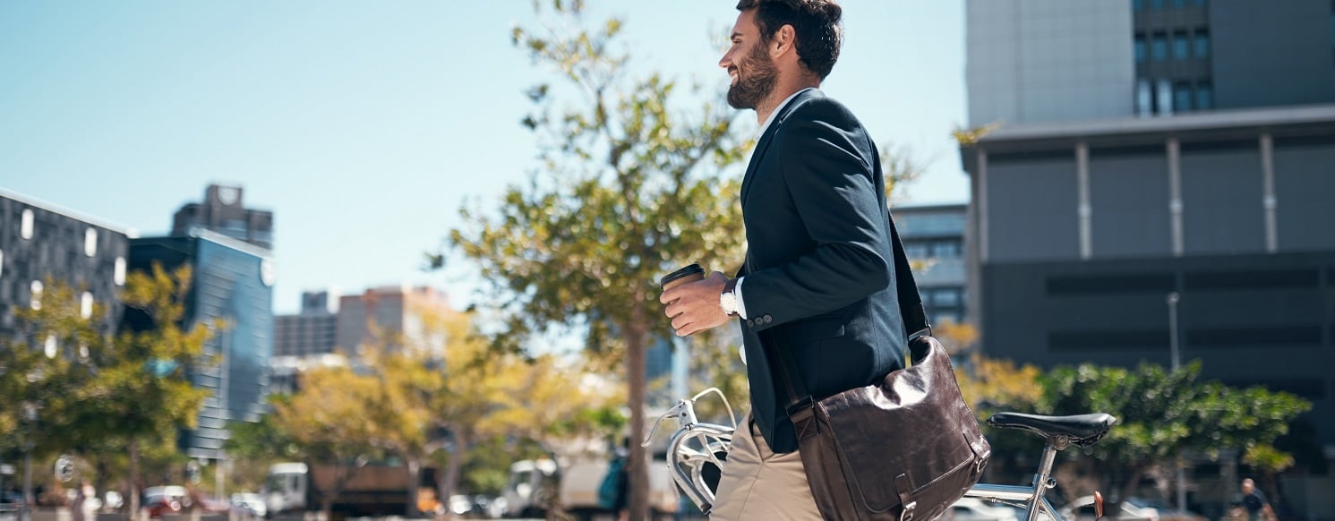 Man outside walking with his bike and holding a coffee