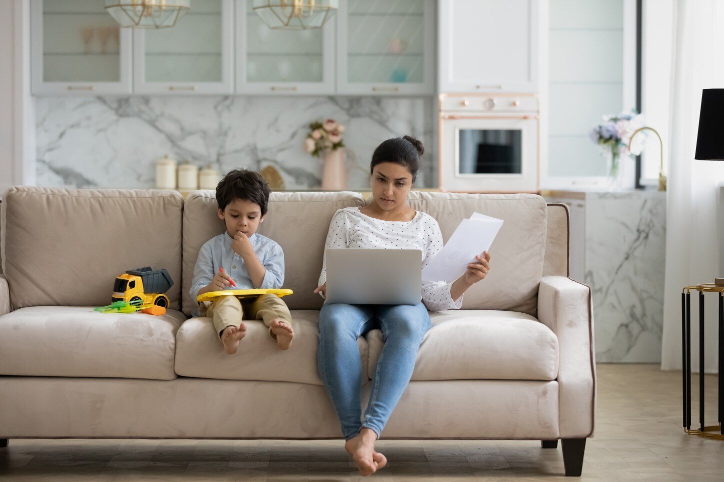 Woman sitting on couch with child and laptop next to her