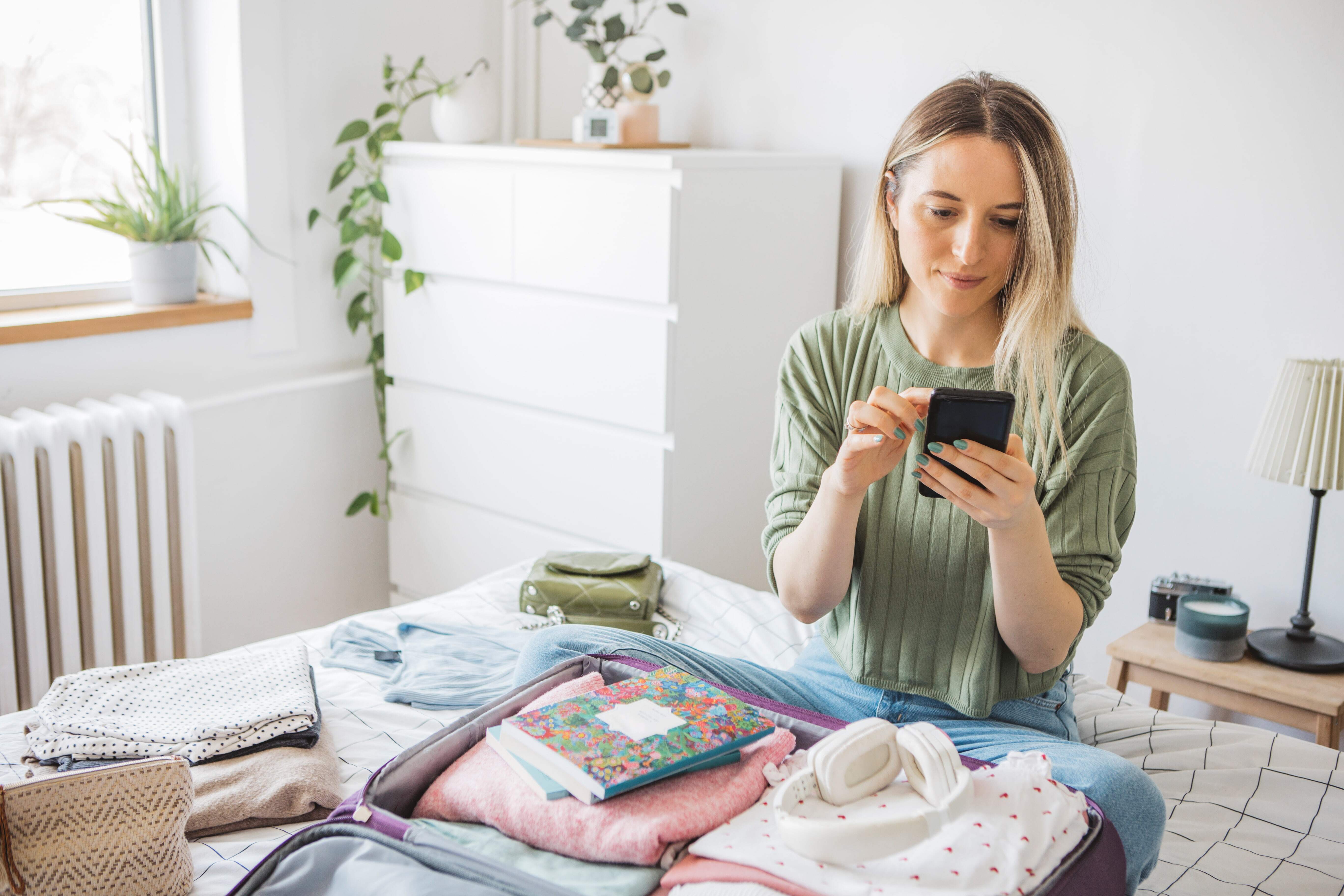 Woman checking phone while packing for a trip