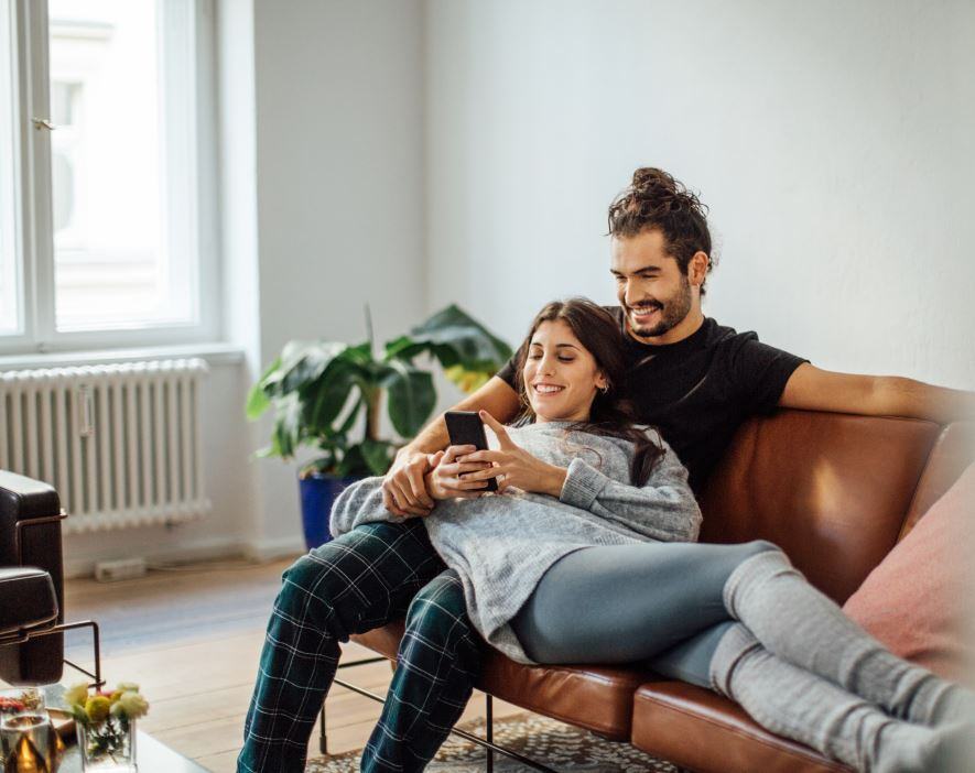 Un homme et une femme sur un canapé regardant un téléphone. L’art de rédiger des textos efficaces: Quelle est la meilleure façon de rédiger des textos clairs?