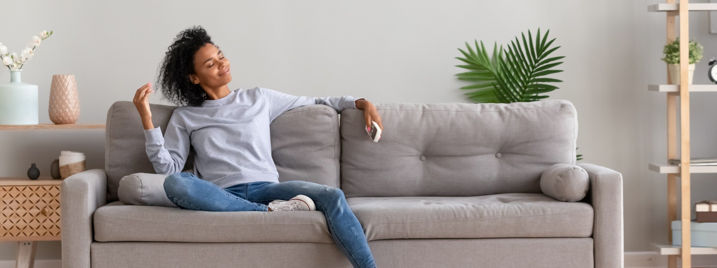 Woman sitting on her couch happy because she's practicing self-love, taking care of her mental and physical well-being.