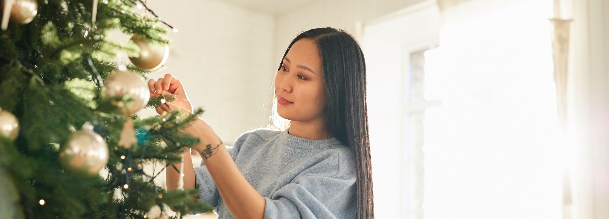 woman decorating the christmas tree in her living room next to the window