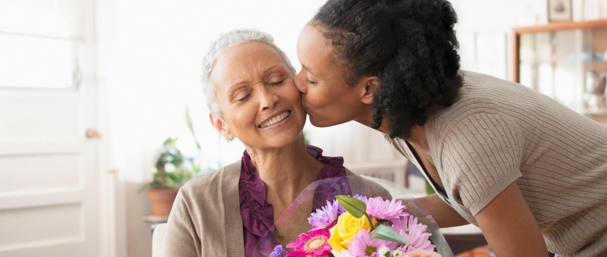 compassionate woman kissing her mother on the cheek and offering her flowers