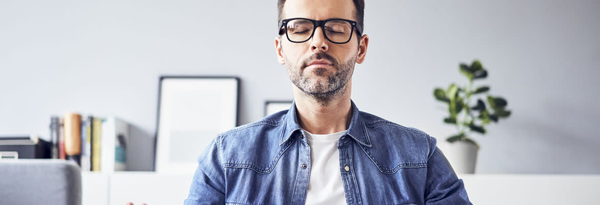 Un homme à lunettes qui médite sur le canapé.