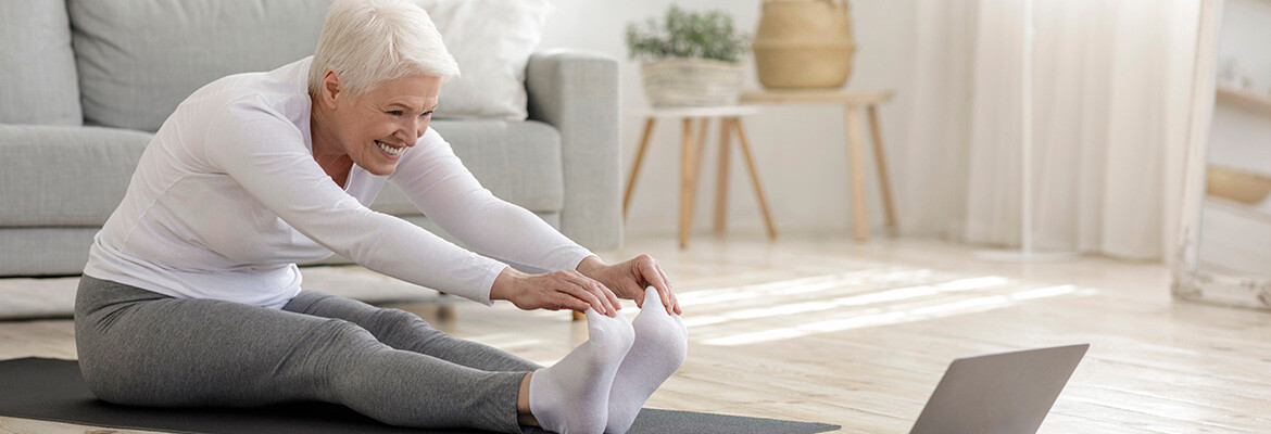 An older woman stretching on the floor of a modern apartment