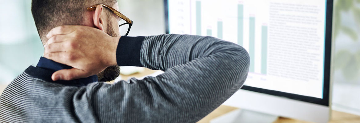 Un homme travaillant sur un ordinateur se frotte le cou.