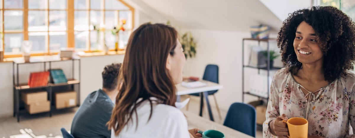 Deux femmes conversent dans un bureau à aire ouverte.