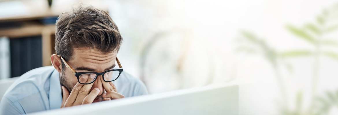 A man rubbing his eyes in front of a computer screen