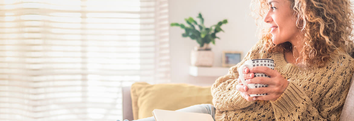 A woman sitting cozily on the couch with a mug of tea