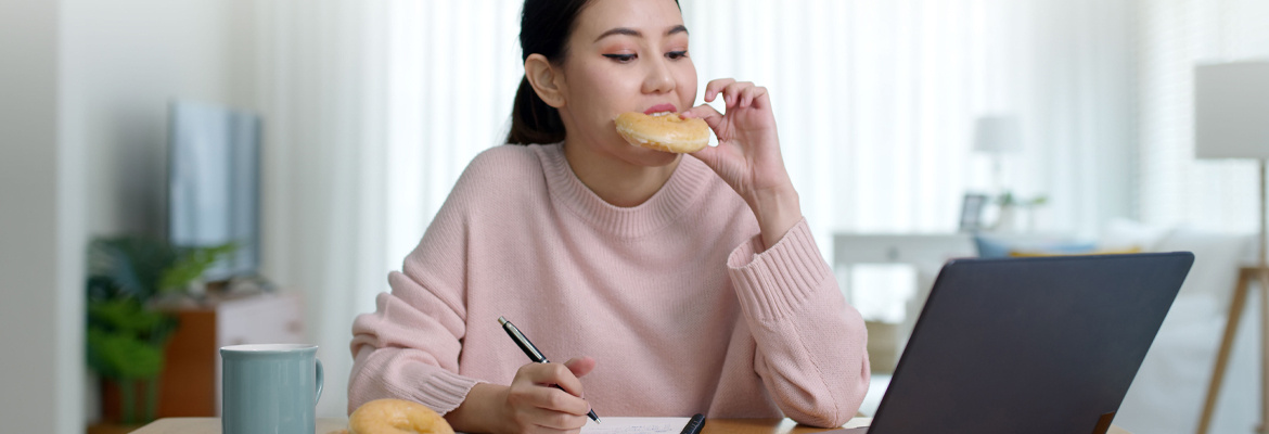 Une femme qui grignote un beignet en travaillant à son bureau.