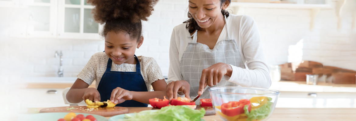 A mother and her daughter cutting vegetables for a salad.