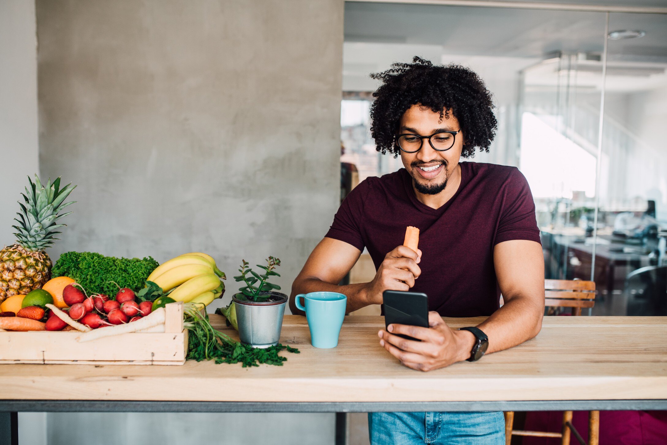 man standing in office kitchen eating carrot