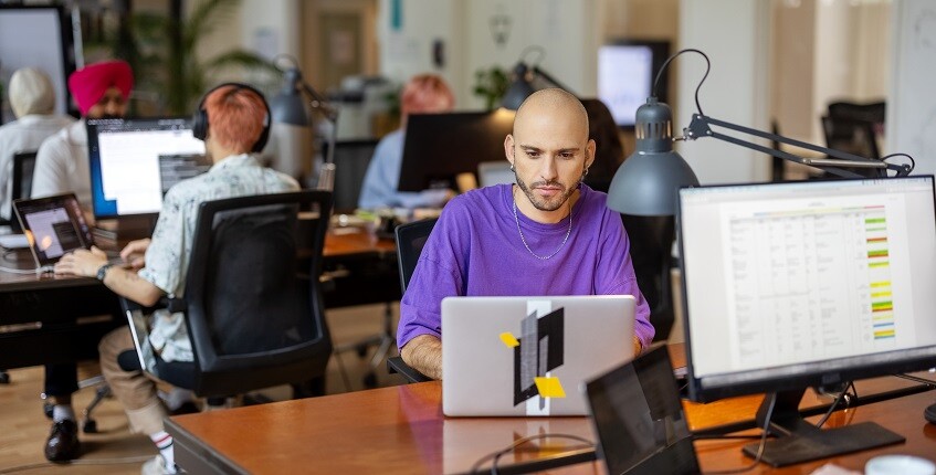 Man in open office sitting at desk with laptop