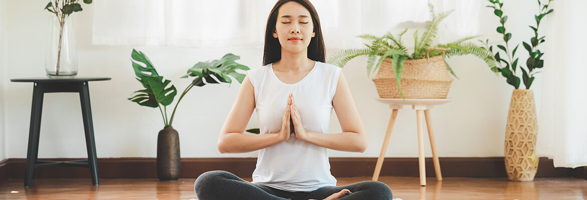 A young woman meditating on the floor in a room decorated with zen plants