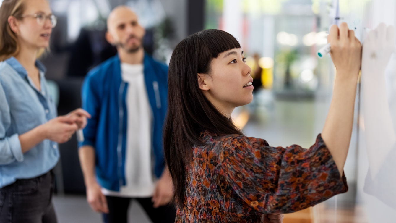 Une femme écrit sur un tableau blanc sous le regard de ses collègues