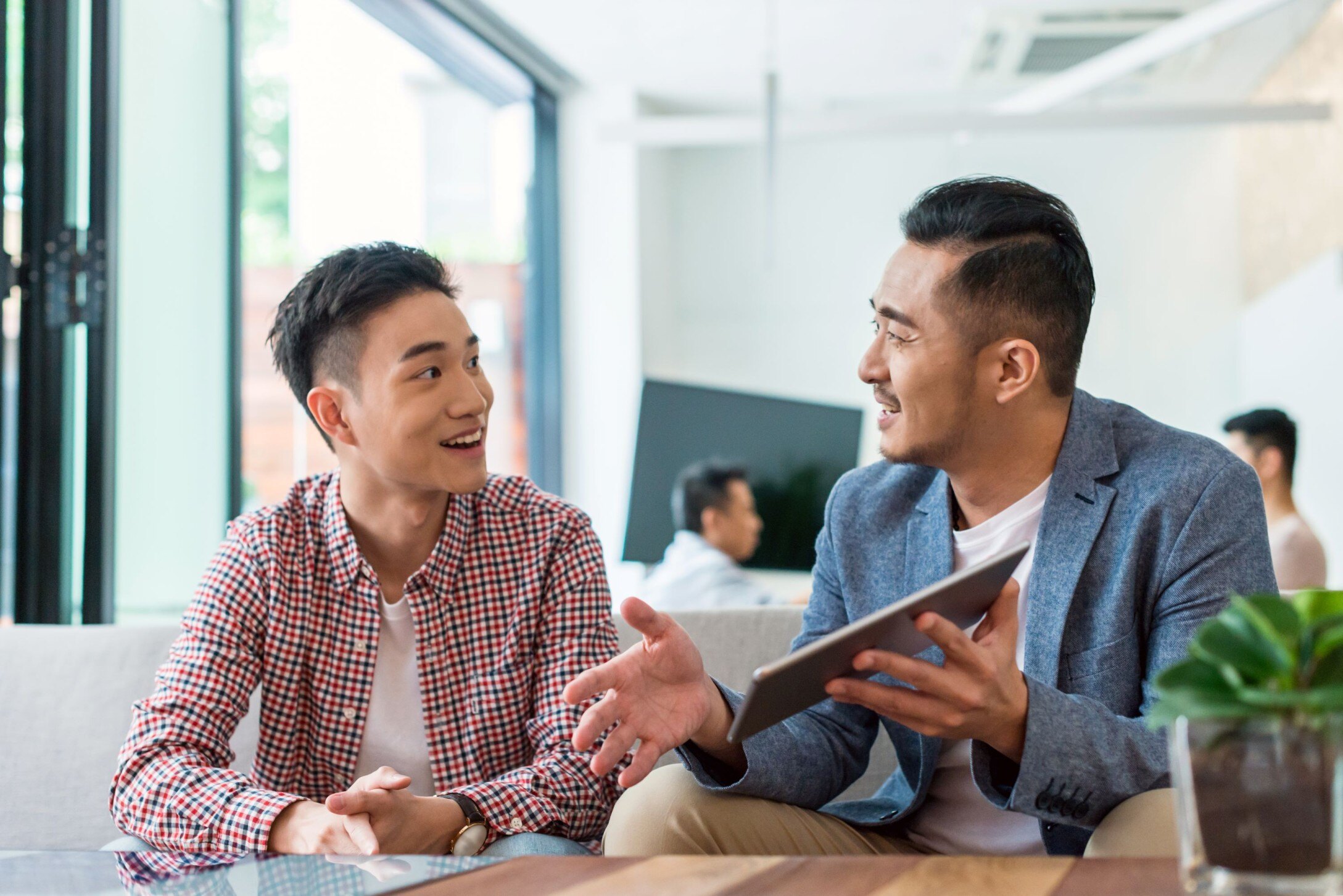 Deux hommes, assis sur un canapé, regardent une tablette.